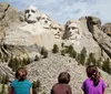 Three individuals are observed from behind gazing upon the iconic Mount Rushmore National Memorial which features the monumental carvings of the faces of four US presidents
