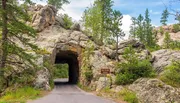 The image shows a road passing through a natural rock tunnel with a sign indicating 