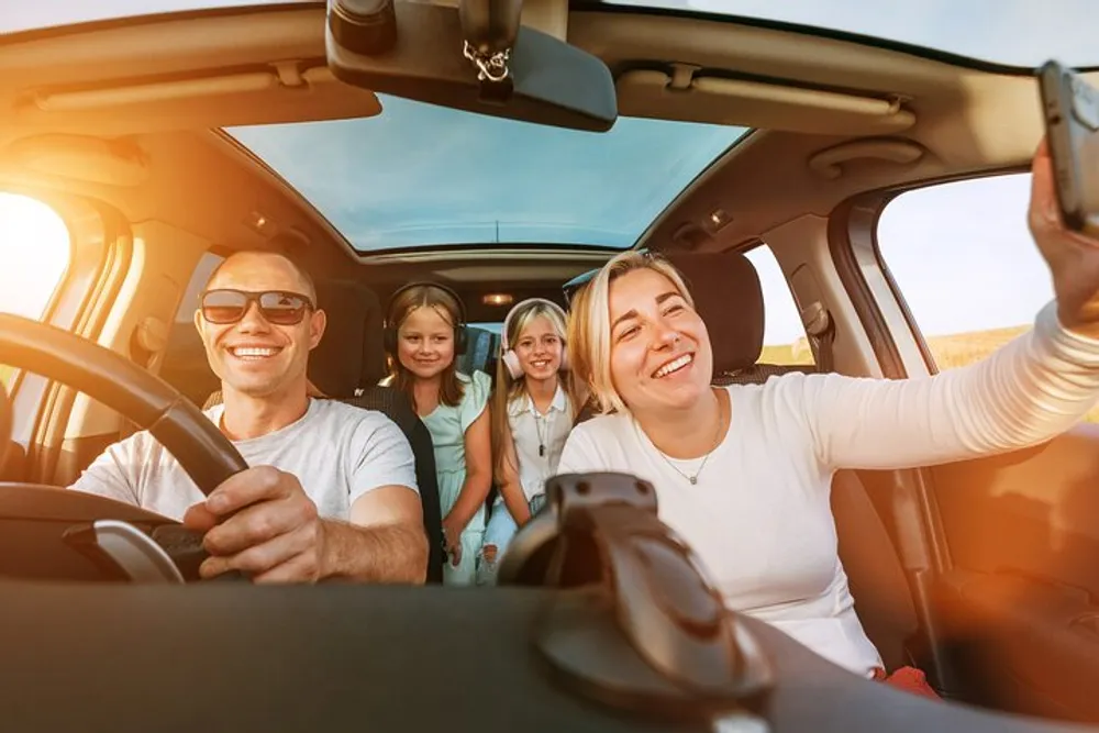 A cheerful family is taking a selfie together inside a car with smiles all around indicating a joyful moment during a road trip or outing