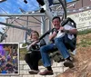 Two people are smiling and enjoying a ride on an alpine coaster near a sign advertising All You Can Eat Pancakes