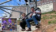 Two people are smiling and enjoying a ride on an alpine coaster near a sign advertising 