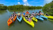 A group of people are enjoying a sunny day kayaking in calm waters surrounded by greenery.