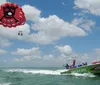 A brightly colored speedboat with a shark face design is towing two people on a parasail above a clear blue sea