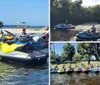 A group of people wearing life vests are posing with their personal watercraft on a sunny day near the shore