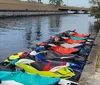 A group of people wearing life vests are posing with their personal watercraft on a sunny day near the shore