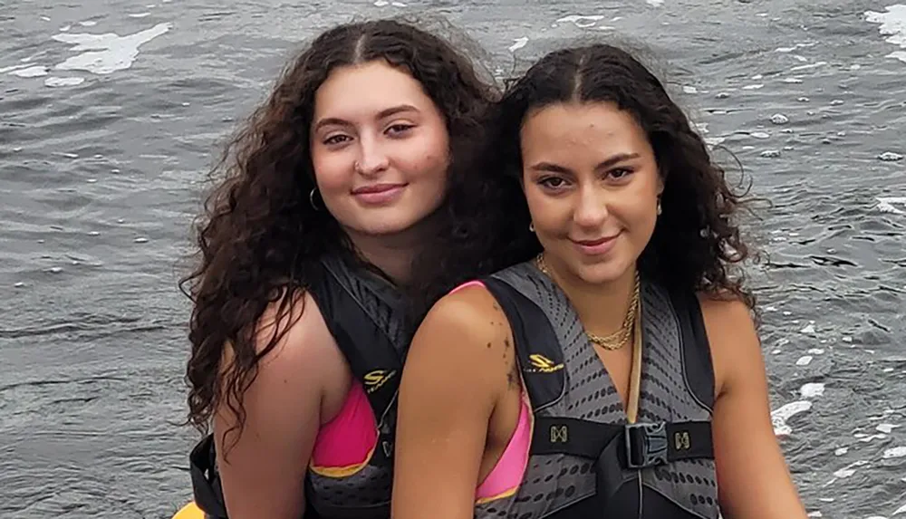 Two people are smiling for the camera while wearing life jackets near water