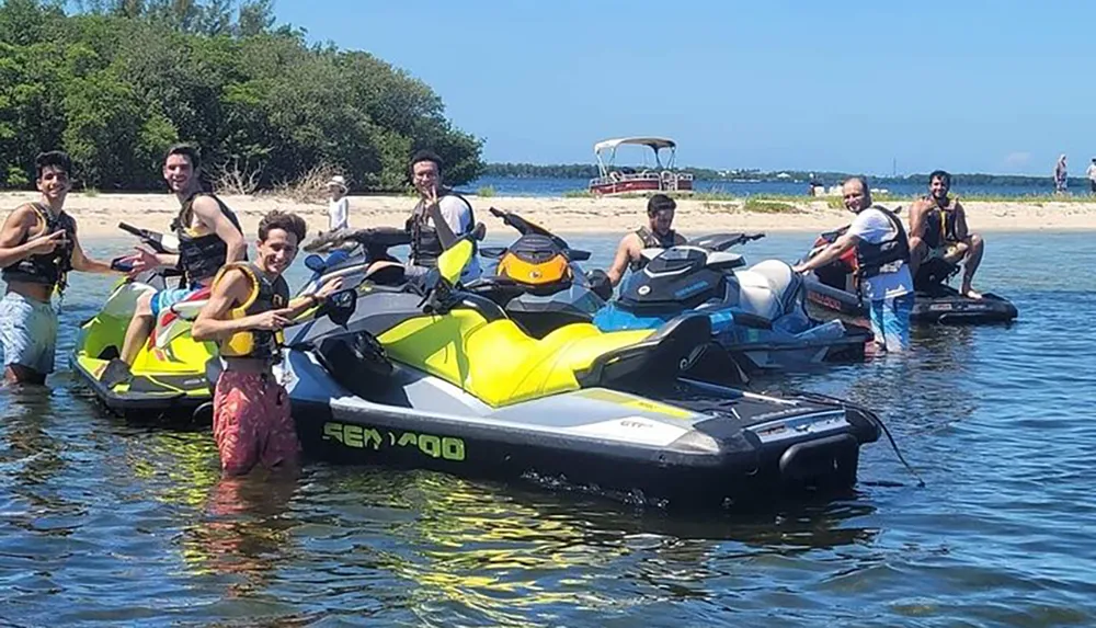 A group of people wearing life vests are posing with their personal watercraft on a sunny day near the shore