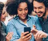 Two people are smiling and looking at a smartphone together with a backdrop of urban architecture