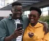 Two people are smiling and looking at a smartphone together with a backdrop of urban architecture