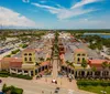 The image shows a sunny outdoor shopping area with a central fountain flanked by palm trees and storefronts including US Polo Assn and Converse with people casually walking by