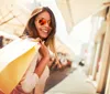 The image shows a sunny outdoor shopping area with a central fountain flanked by palm trees and storefronts including US Polo Assn and Converse with people casually walking by