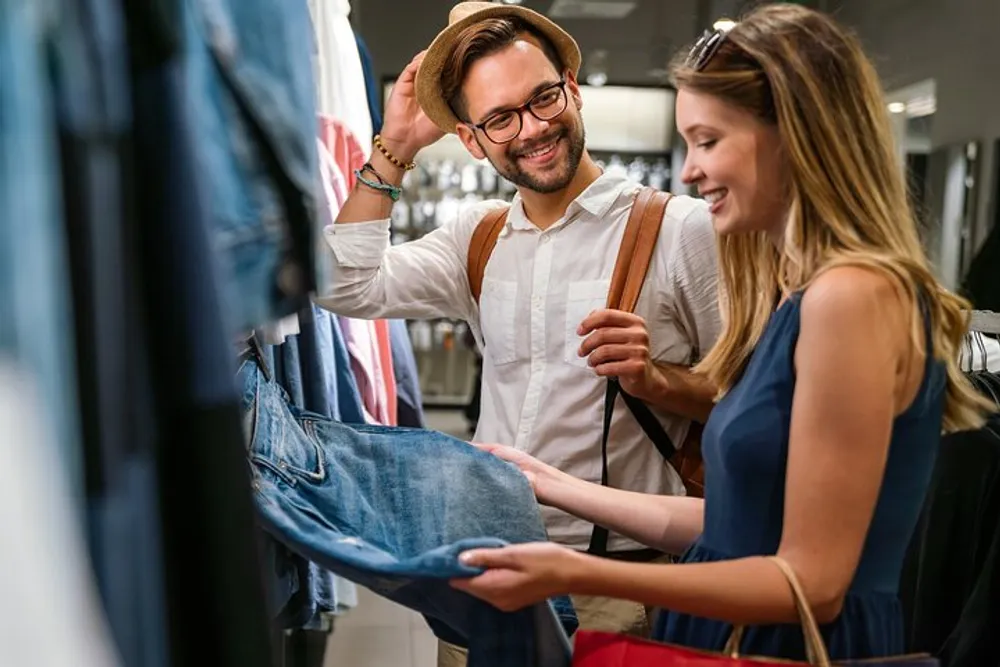 A man and a woman are smiling and examining a pair of jeans in a clothing store