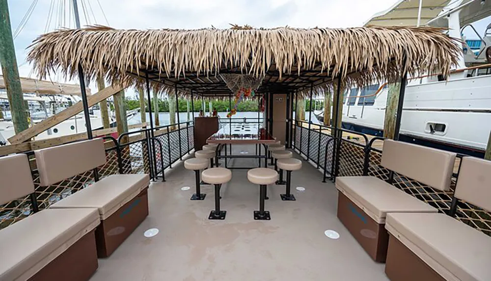 The image shows a tiki bar-themed floating deck with stools and benches netted railings and a thatched roof possibly docked at a marina