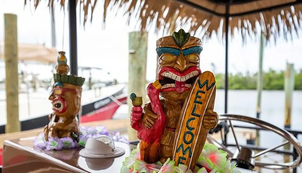 The image features colorful tiki statues holding a WELCOME sign at a tropical-themed bar with a view of the water and a boat steering wheel in the foreground