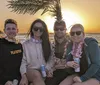 Four friends are enjoying a sunset together on a beach wearing flower necklaces and holding drinks