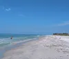 This image showcases a serene beach scene with a clear blue sky gentle waves and people enjoying leisure time by the water