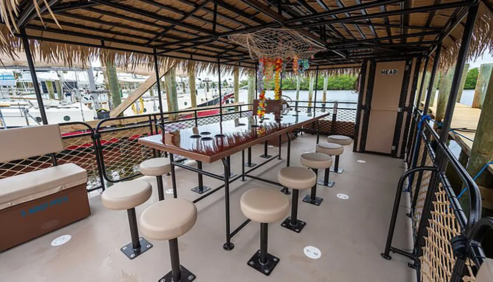 The image shows a covered outdoor bar area with stools and a thatched roof overlooking a marina with boats in the background