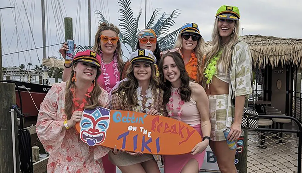 A group of people in colorful attire holding a sign that says Gettin Freaky on the Tiki are posing happily for a photo