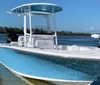 A center console boat painted in light blue and white is anchored near the shore under a clear sky