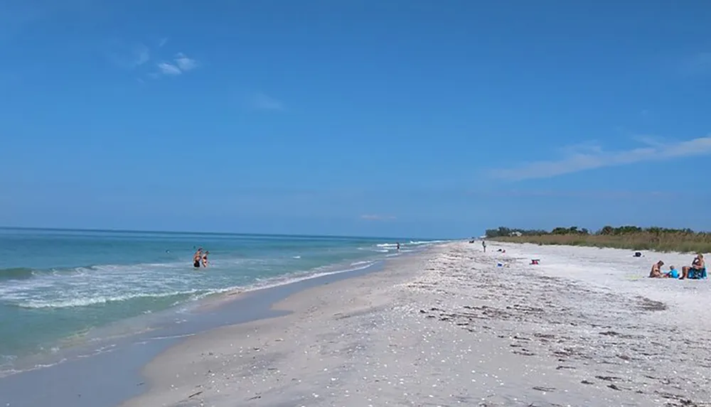 The image showcases a serene beach scene with a clear blue sky calm ocean waters and several beachgoers enjoying the sun and sand