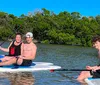 Three people are enjoying paddle boarding on a calm water body with lush greenery in the background