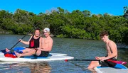 Three people are enjoying paddle boarding on a calm water body with lush greenery in the background.