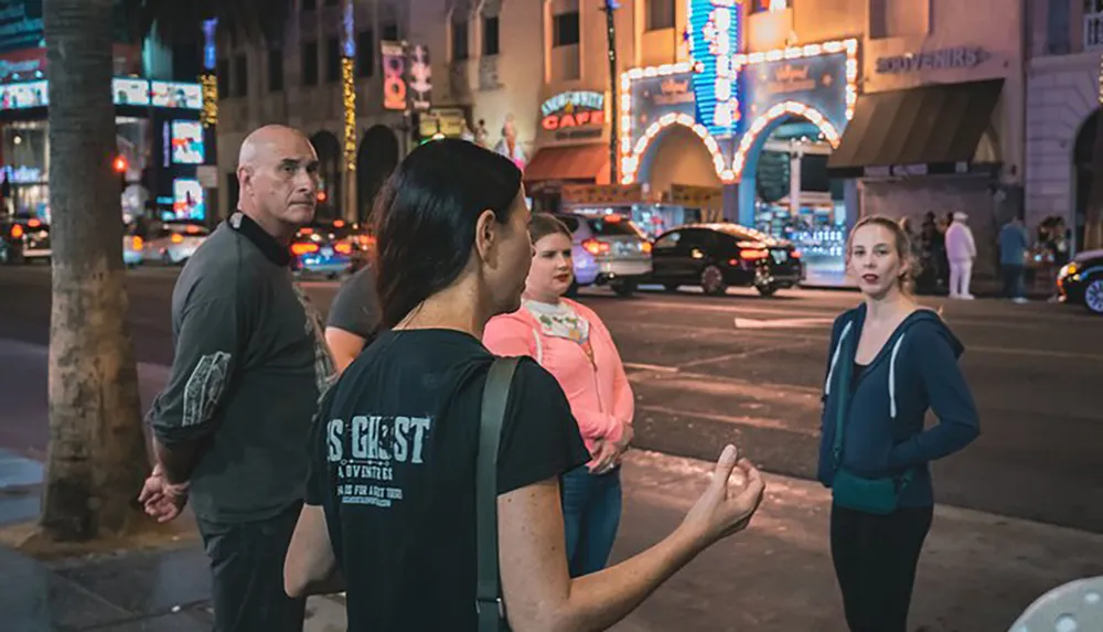 This image captures a moment on a bustling city street at night where a group of people appear engaged in a conversation against a backdrop of neon signs and urban activity