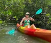 Two people are smiling while kayaking among mangroves both holding blue paddles and wearing sun hats