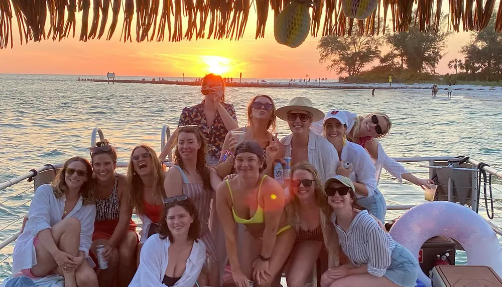 A group of happy people are enjoying a sunset boat ride near a beach with drinks in hand exuding a warm lively atmosphere