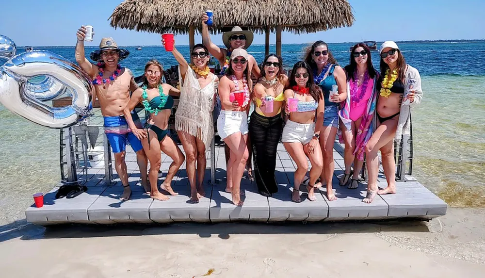 A group of joyful people are posing on a beach dock with drinks in their hands celebrating under a clear blue sky