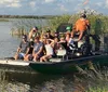 A group of people is enjoying a ride on an airboat in a wetland environment with some passengers waving at the camera