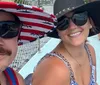 Two people are smiling for a selfie on a boat wearing sunglasses and wide-brimmed hats
