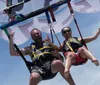Two people are ecstatically enjoying a parasailing adventure against a blue sky