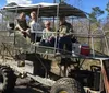 Four individuals are sitting on a large open-air swamp buggy vehicle in a wooded area