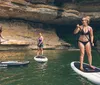 Four individuals are standing on paddleboards engaging in an activity near a rocky cliff with a small waterfall