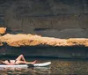 Four individuals are standing on paddleboards engaging in an activity near a rocky cliff with a small waterfall