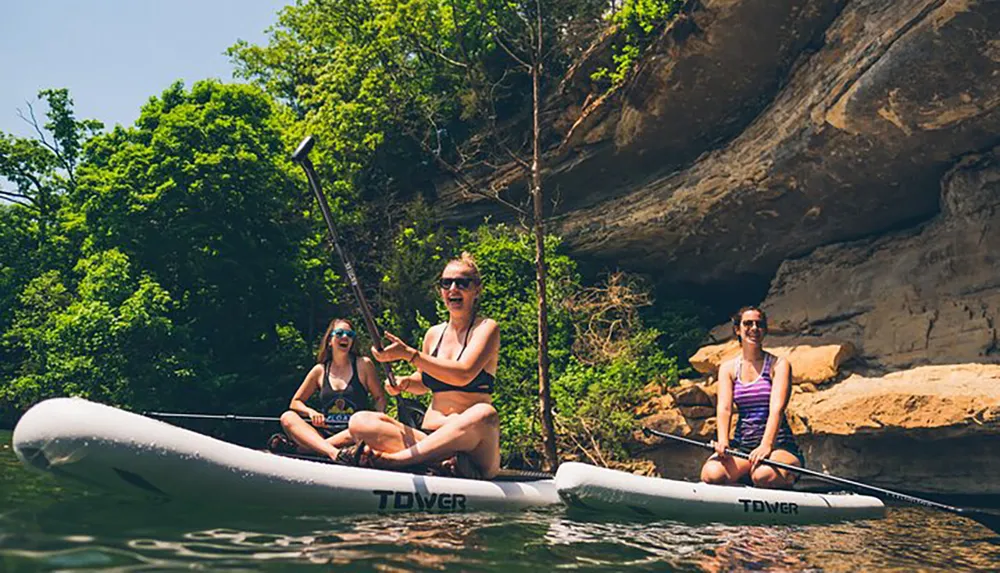 Three individuals are enjoying stand-up paddleboarding on a calm body of water surrounded by natural scenery