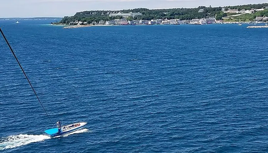 A speedboat is cruising on the blue waters near a coastline dotted with buildings under a clear sky.