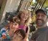 A family of four is smiling for a selfie on a sunny day on a city sidewalk