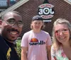 A family of four is smiling for a selfie on a sunny day on a city sidewalk