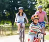 A child leads the way on a bike ride with two adults cycling behind on a sunny tree-lined path