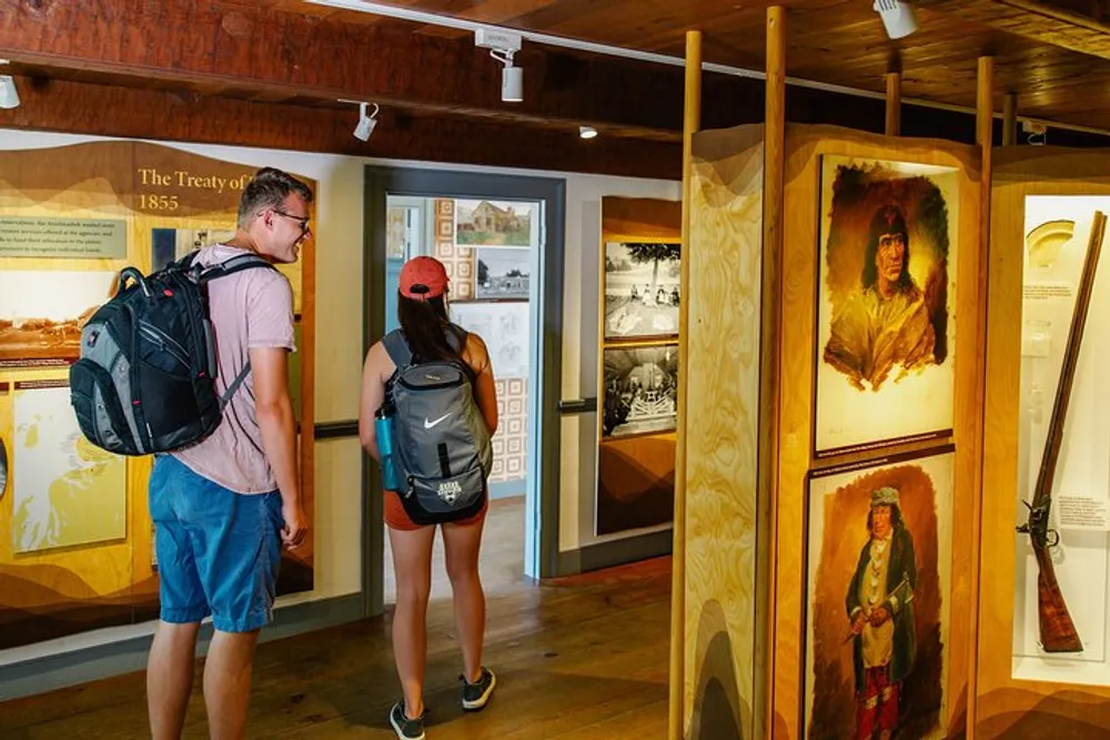 Two people with backpacks are observing exhibits at a history museum