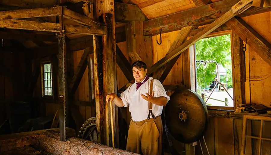 A person in period attire is giving a demonstration or speaking inside an old-fashioned workshop with traditional woodworking tools and materials.