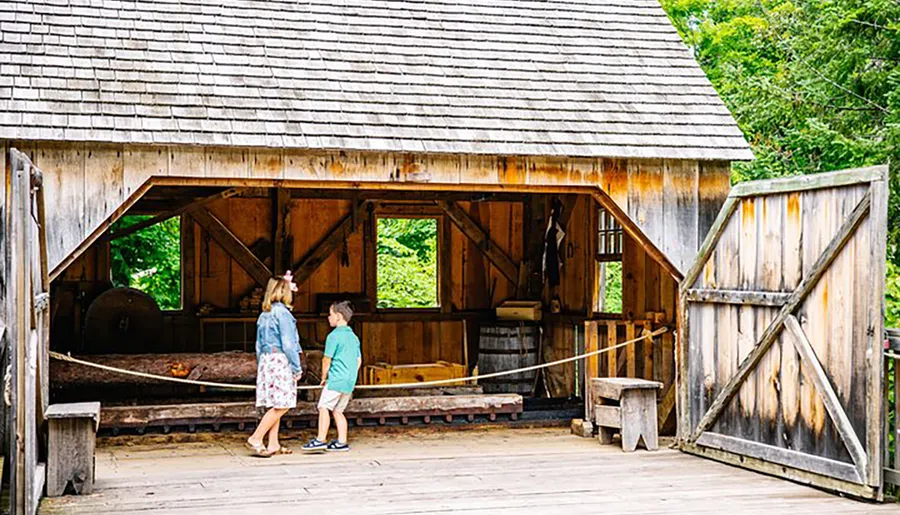 Two people are talking near the open entrance of a rustic wooden building that appears to be a historical or heritage site.