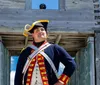 Individuals dressed in historical military uniforms stand beside a cannon with a large suspension bridge in the background