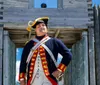 Individuals dressed in historical military uniforms are standing next to a cannon with a modern suspension bridge in the background