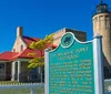 A couple is enjoying a sunny day outdoors while the man points at a historic lighthouse and adjacent building possibly discussing the site or preparing to take a photo