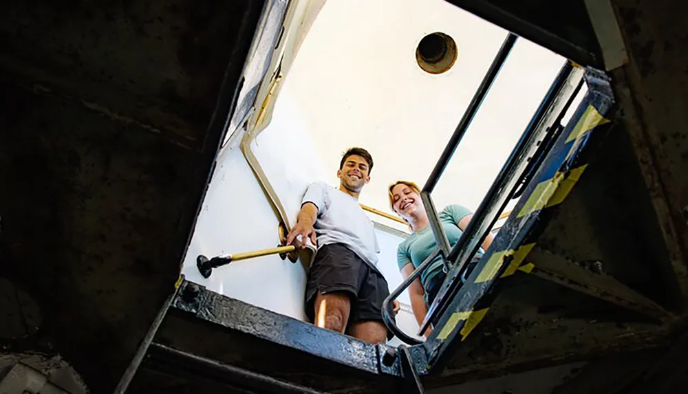 A man and a woman are smiling while ascending a rugged metal staircase