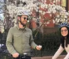 Three people wearing bicycle helmets are posing for a photo with a backdrop of the Brooklyn Bridge and New York City skyline