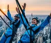 Two individuals in safety harnesses are gleefully experiencing an urban high-altitude adventure against a backdrop of a city skyline at sunset